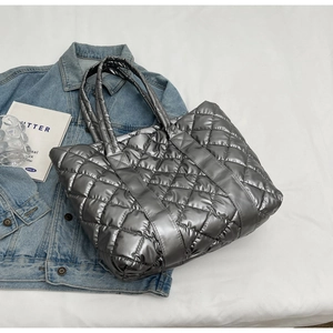 Close-up of silver quilted tote bag with metallic finish on white bedding backdrop