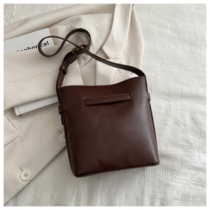 Flat lay of a coffee brown bucket bag with adjustable strap on a cream blazer