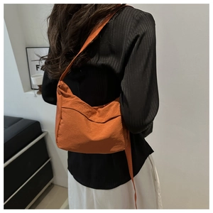 Detail of orange nylon crossbody tote bag showing front pocket and slim shoulder strap