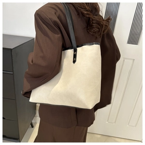 Detail of minimalist beige tote bag with black trim worn with a brown blazer suit