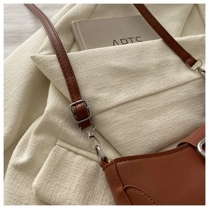 Détail des coutures du sac en cuir marron et boucle en métal argenté sur un blazer