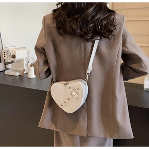 Detail of cream heart-shaped crossbody bag featuring buckle straps and silver studs