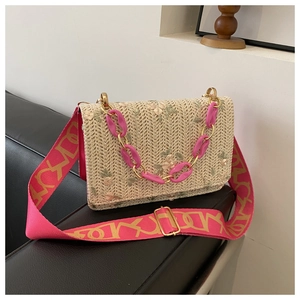 Détail d'un sac en paille avec broderie florale et bandoulière en tissu rose
