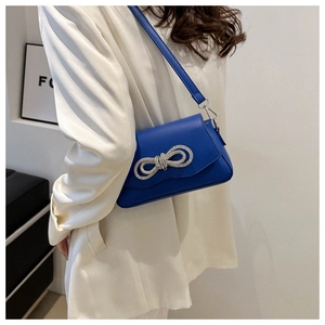 Detail of royal blue leather shoulder bag featuring a large sparkling rhinestone bow
