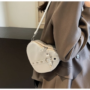 Detailed shot of white heart-shaped crossbody bag featuring silver studs and buckle strap