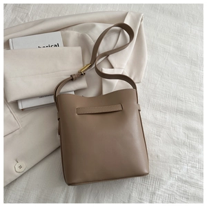 Detailed macro view of tan leather bucket bag with bronze hardware on white fabric