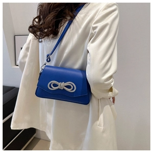 Royal blue shoulder bag with rhinestone bow detail worn by a model in a white suit