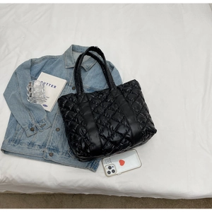 Close-up of black quilted puffer tote bag with large diamond texture on white fabric
