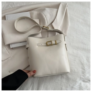 Close-up of cream leather bucket bag featuring brushed gold metal hardware and strap