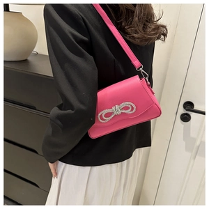 Detail of a shiny pink shoulder bag featuring a sparkling silver rhinestone bow decoration