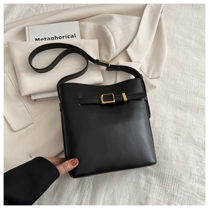 Detail of black leather bucket bag with gold buckle on a beige suit background
