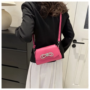 Hot pink crossbody bag with rhinestone bow detail worn over a black blazer for chic styling