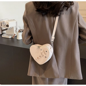 Detail of cream heart-shaped crossbody bag with silver studs and adjustable strap on a model