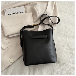 Detail of minimalist black matte leather bucket bag with adjustable gold metal buckle strap