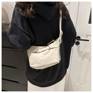 Detailed back view of a minimalist beige crescent crossbody bag worn by a model