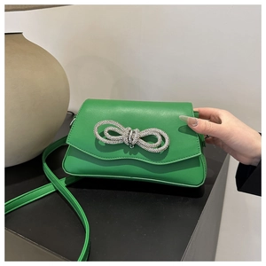 Close-up of green leather square bag featuring a large sparkling rhinestone bow detail