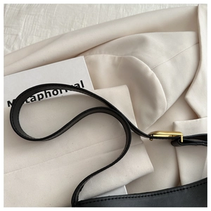 Close-up of black matte leather shoulder bag featuring vintage gold metal buckle and stitching