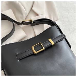 Detail of black leather bucket bag with vintage bronze buckle on white blazer