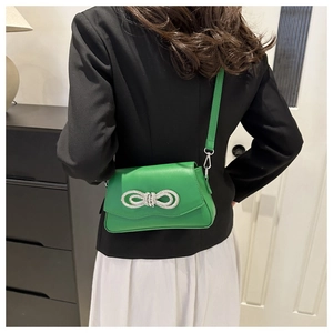Close-up of a green crossbody bag with a sparkling rhinestone bow on a female model