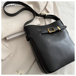 Detail of black leather bucket bag featuring gold hardware on a white blazer