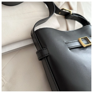 Detail view of the black leather bucket bag showing stitching and vintage gold metal buckles