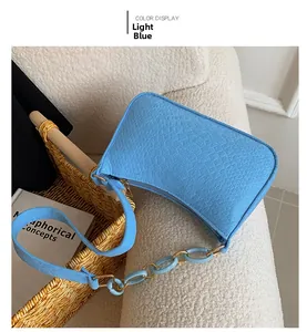 Detail of light blue crossbody bag with crocodile texture on white velvet surface