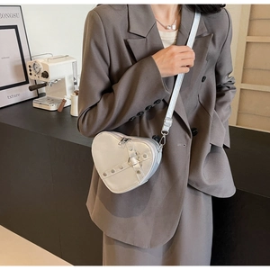 Silver heart-shaped crossbody bag with metallic finish and decorative straps on model