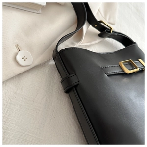 Detail of black matte leather bucket bag with gold metal buckle and neat stitching