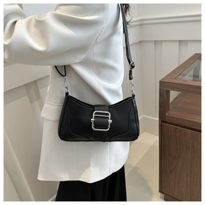 Détail d'un sac baguette en cuir noir avec boucle argentée porté sur un blazer blanc