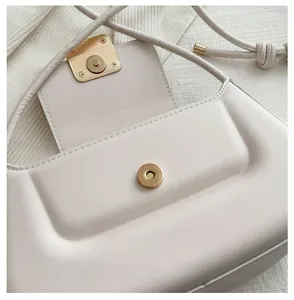 Detail of light gold magnetic clasp on off-white leather shoulder bag with sleek finish