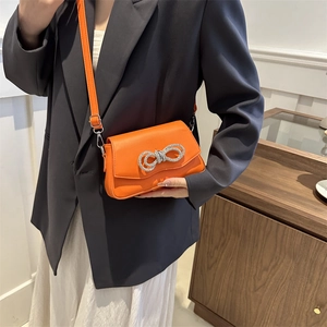 Bright orange mini shoulder bag with rhinestone bow buckle worn by a model