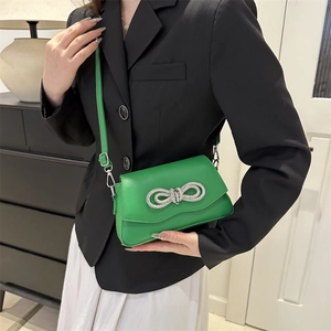 Vibrant green crossbody bag with rhinestone bow detail worn by a model in a black suit