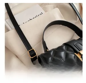 Detail of black quilted crossbody bag showing gold metal buckle and leather texture