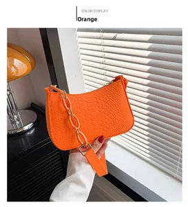 Detail of orange underarm bag with crocodile texture and thick matching chain handle