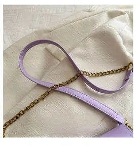 Détail de la bandoulière en cuir lavande avec chaîne dorée sur fond de tissu texturé