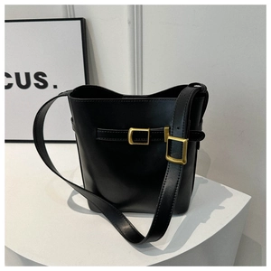 Detail of black leather bucket bag with gold metal buckle on a minimalist white stand