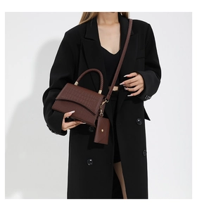 Detail of brown crocodile pattern handbag with braided handle and gold hardware on model