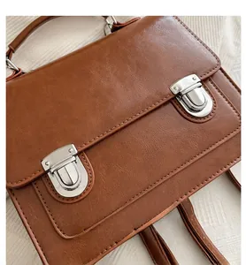 Close-up of brown vintage leather satchel showing metallic buckles and textured finish