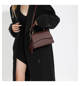 Detail view of brown crocodile-patterned crossbody bag with small pouch charm on a model