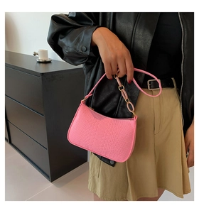 Pink crocodile pattern shoulder bag with gold chain strap detail on a stylish model