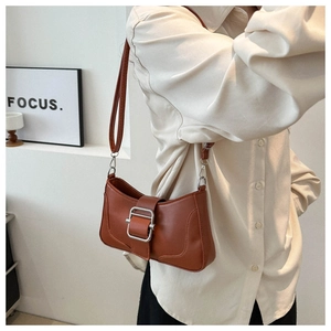 Détail d'un sac baguette marron avec boucle argentée dans un décor urbain minimaliste