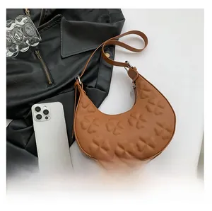 Detail of clover embossed pattern on caramel brown crescent shoulder bag with zipper