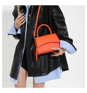 Detail of orange faux leather crossbody bag with crocodile texture and woven handle