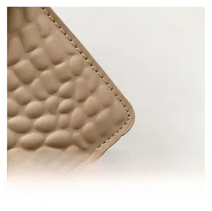 Close-up of beige faux leather with stone texture and fine stitching on the shoulder bag