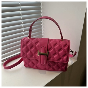 Detail of magenta quilted square bag with gold metallic lock and cross-body strap