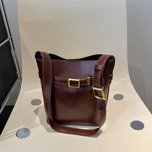 Minimalist coffee brown leather bucket bag with gold hardware on a modern chair