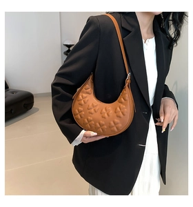 Close-up of brown crescent underarm bag featuring embossed clover patterns on PU leather