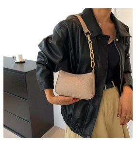 Detail of light beige crescent shoulder bag with chunky metal chain on model