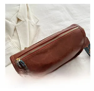 Close-up of brown barrel bag with vintage leather texture and colorful woven strap