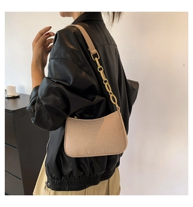 Detail of beige crocodile pattern underarm bag with gold metal chain strap on model